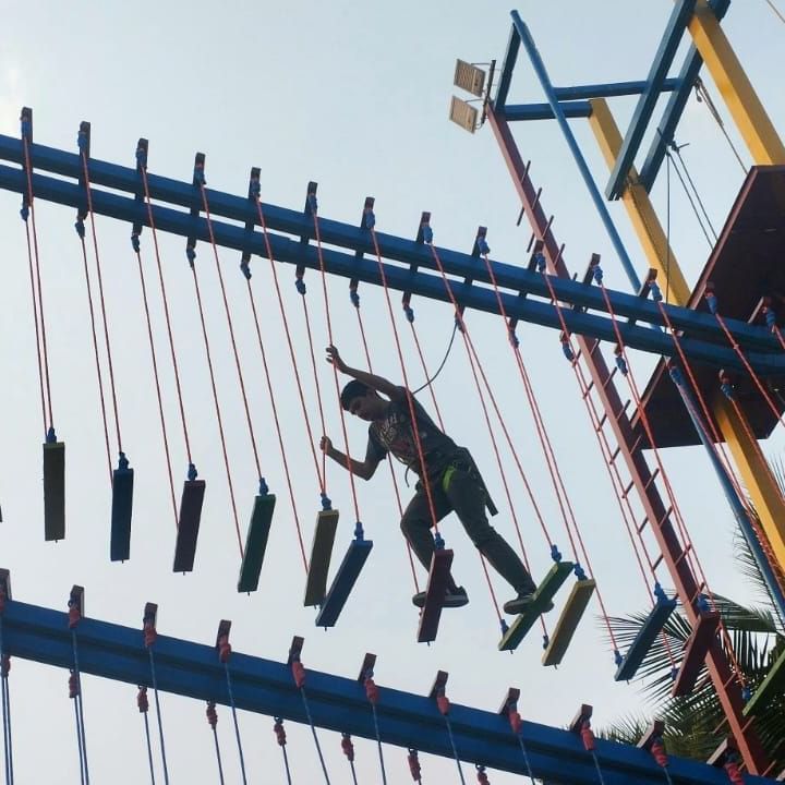Silhouetted figures climb an outdoor adventure course structure with ropes and ladders