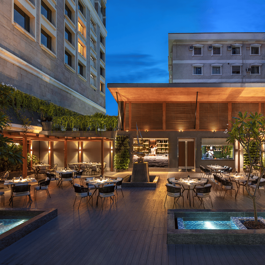 An outdoor dining area with tables, chairs, and plants, illuminated by warm lighting along with swimming pool. 