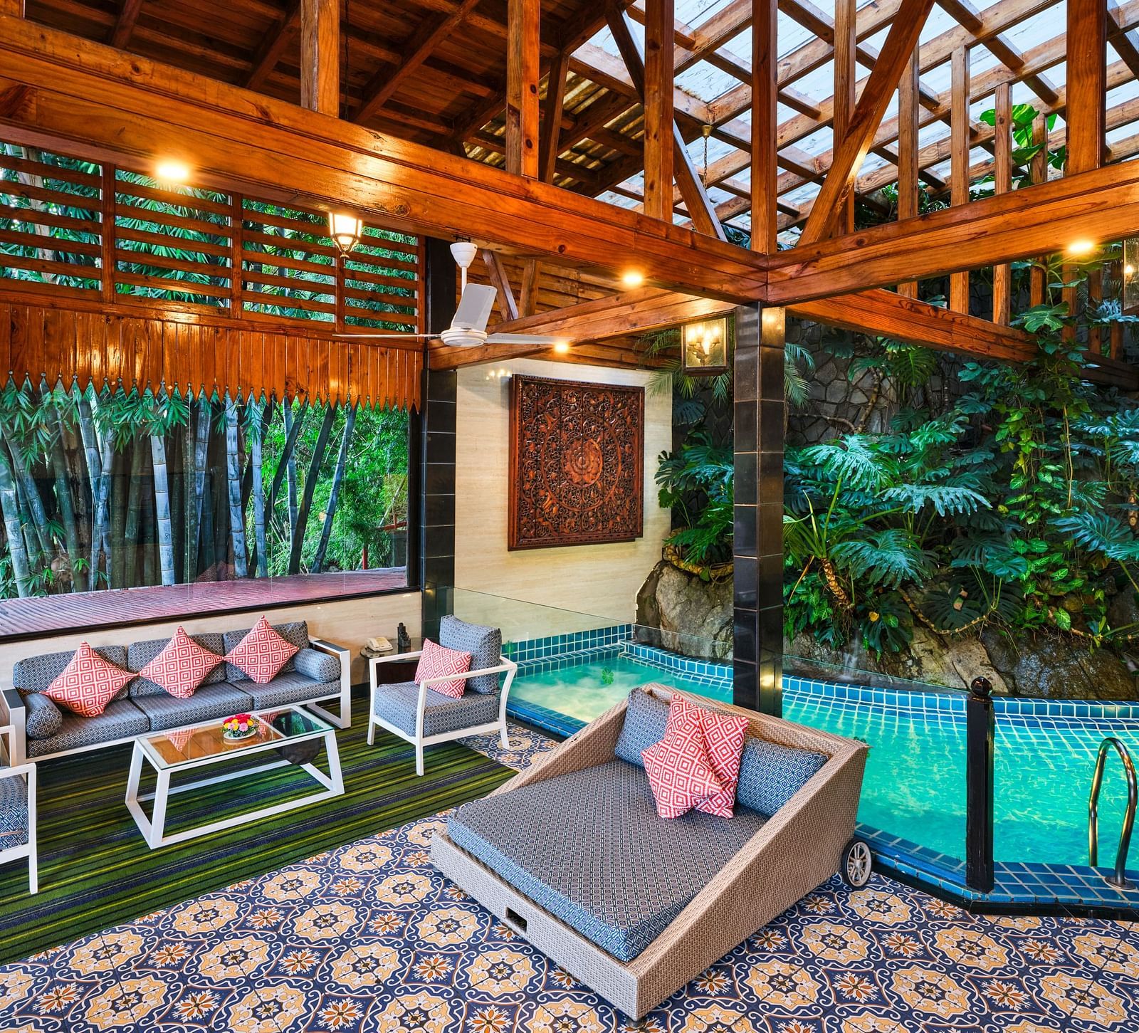 An artistic luxurious outdoor space of Grand Villa featuring a pool, patterned tile floor, outdoor seating, wooden structures, an lush greenery.