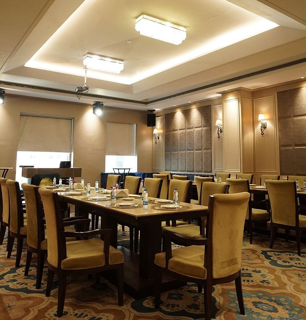 A spacious and modern banquet hall at Nirvana Luxury Hotel, Ludhiana, set with neatly arranged tables and chairs on a patterned blue carpet, ready for an event.