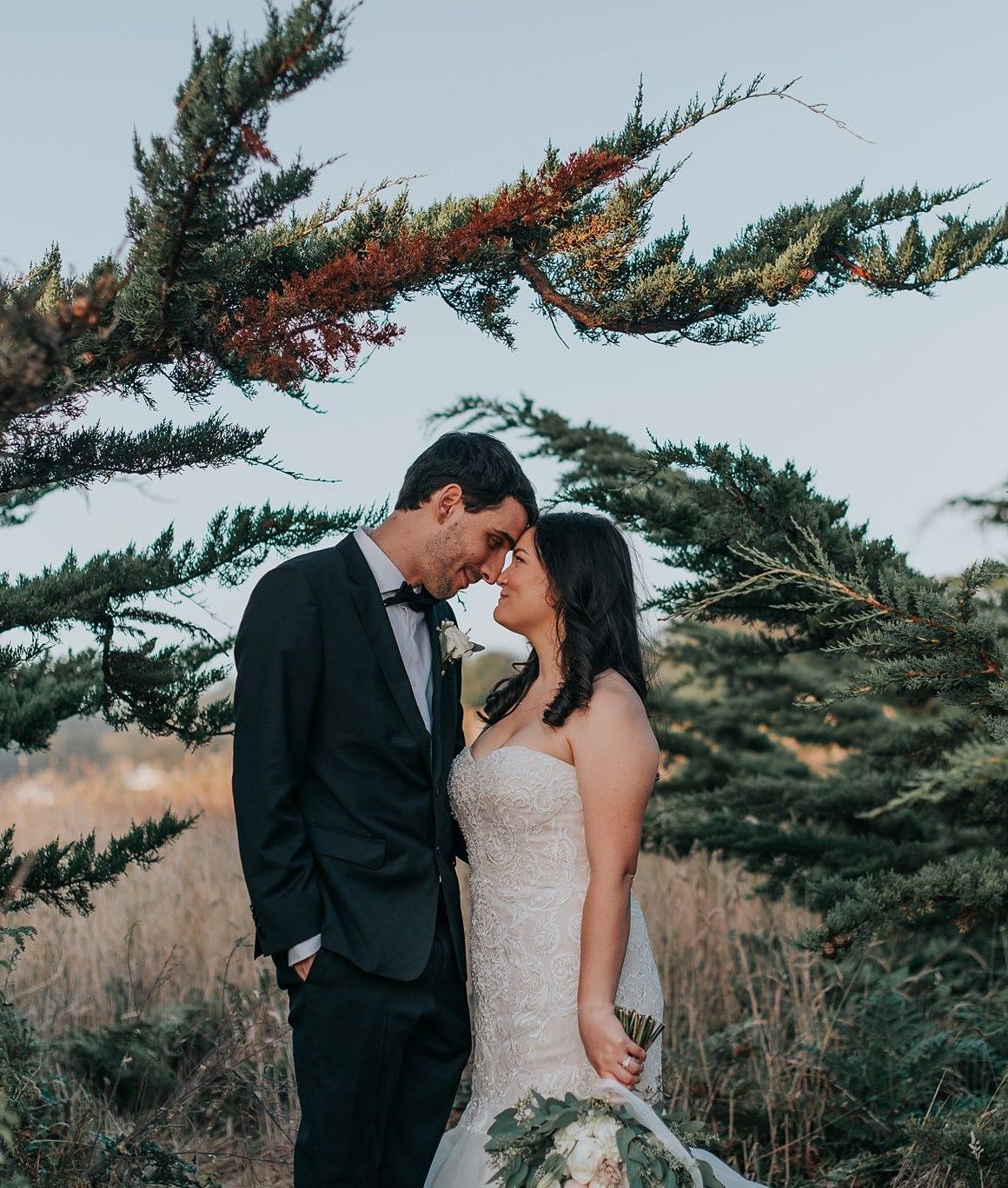 Bride and groom sharing a kiss, framed by lush greenery