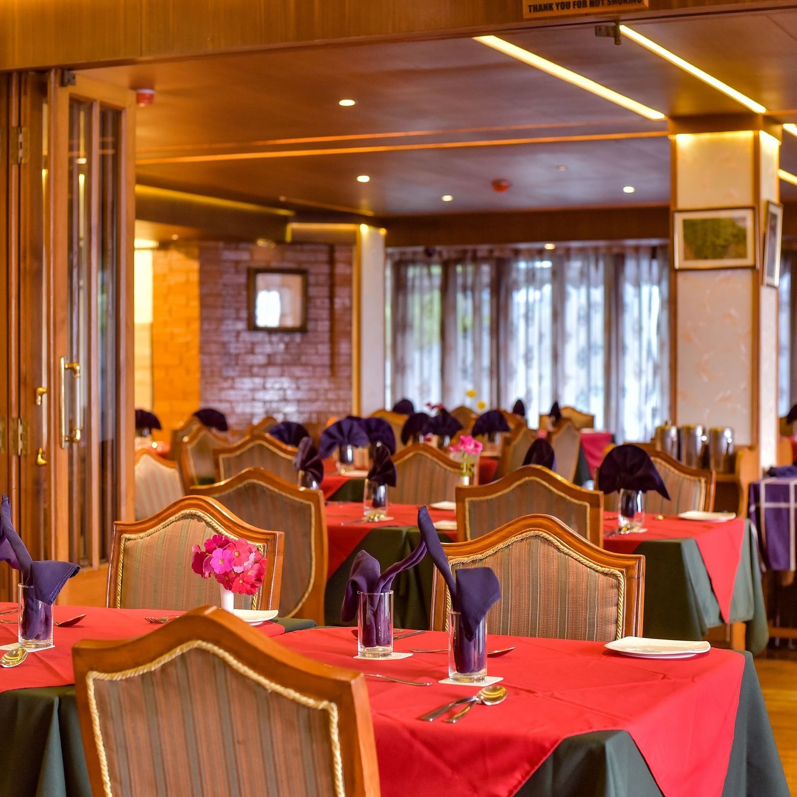 Dining area at Cedar Inn, Darjeeling, featuring elegant wooden interiors, red and green tablecloths, and neatly folded napkins on each table.