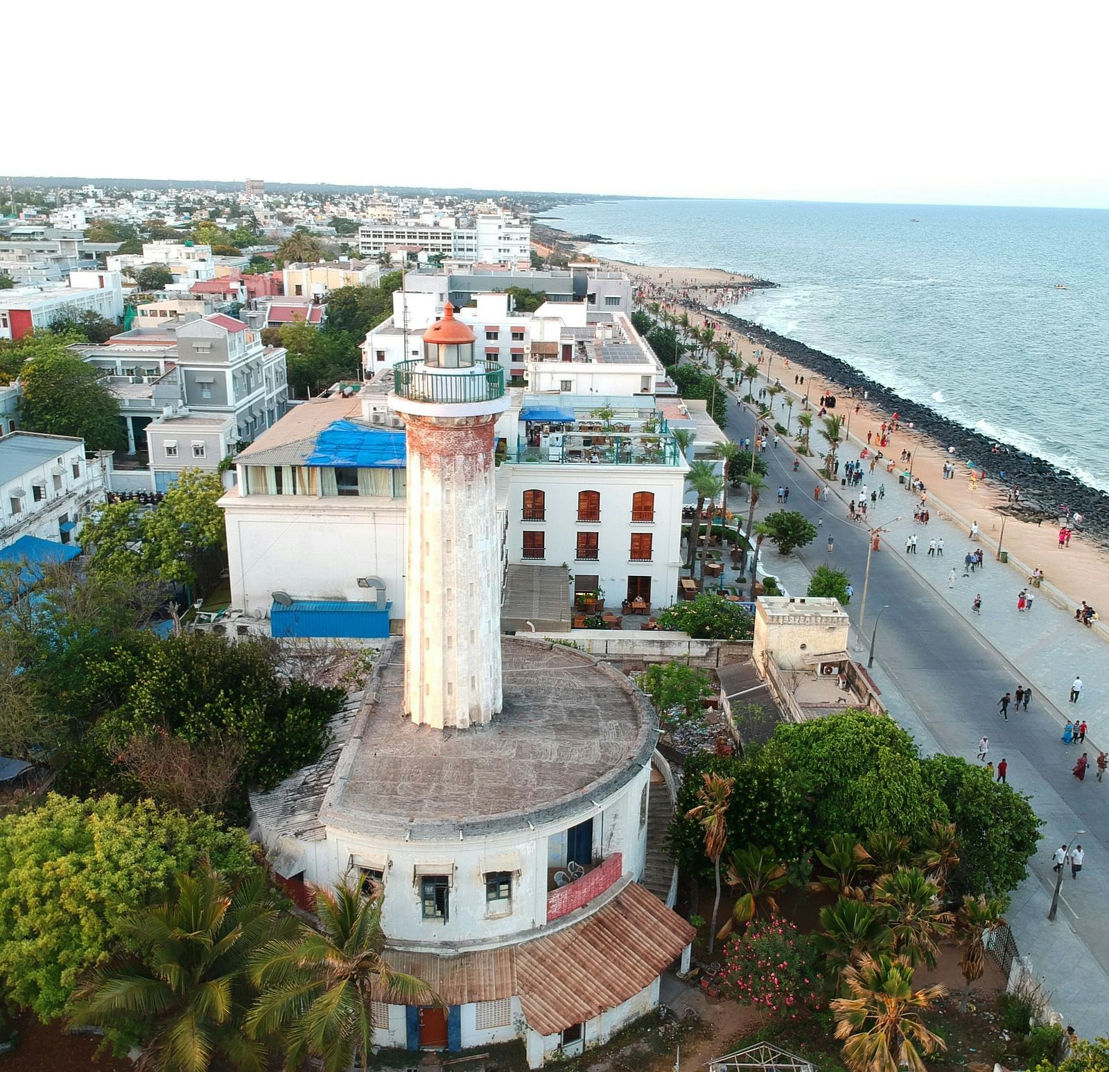 An aerial view of Pondicherry with buildings next to a beach and people walking.