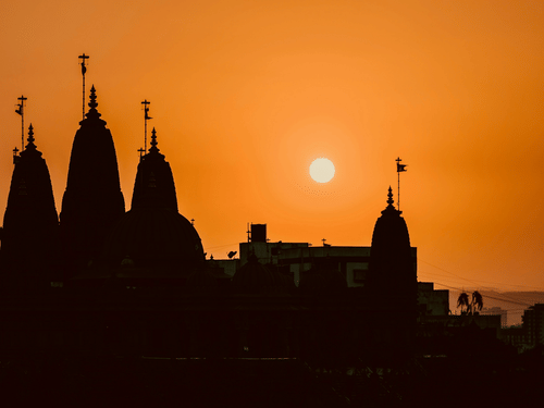Silhouette of temple spires and buildings with the sun low in the sky behind them.