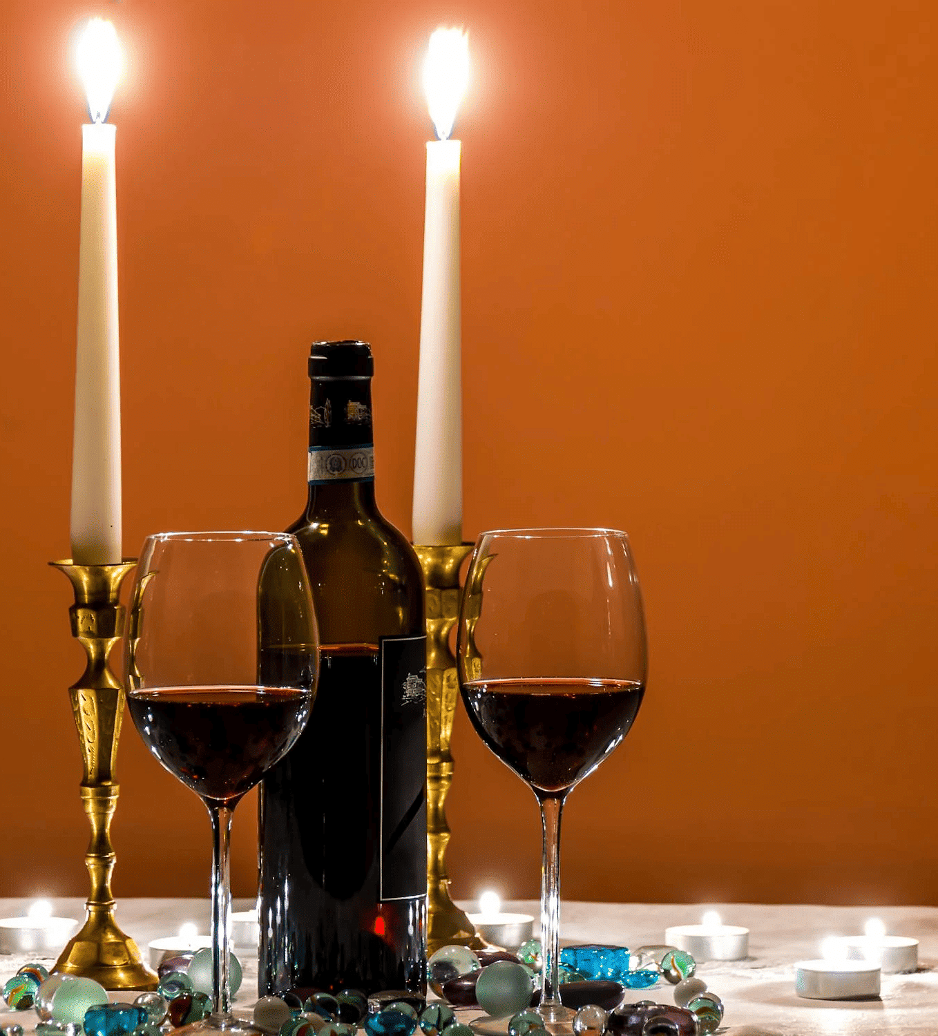 Image of two wine glasses with two candles behind it.