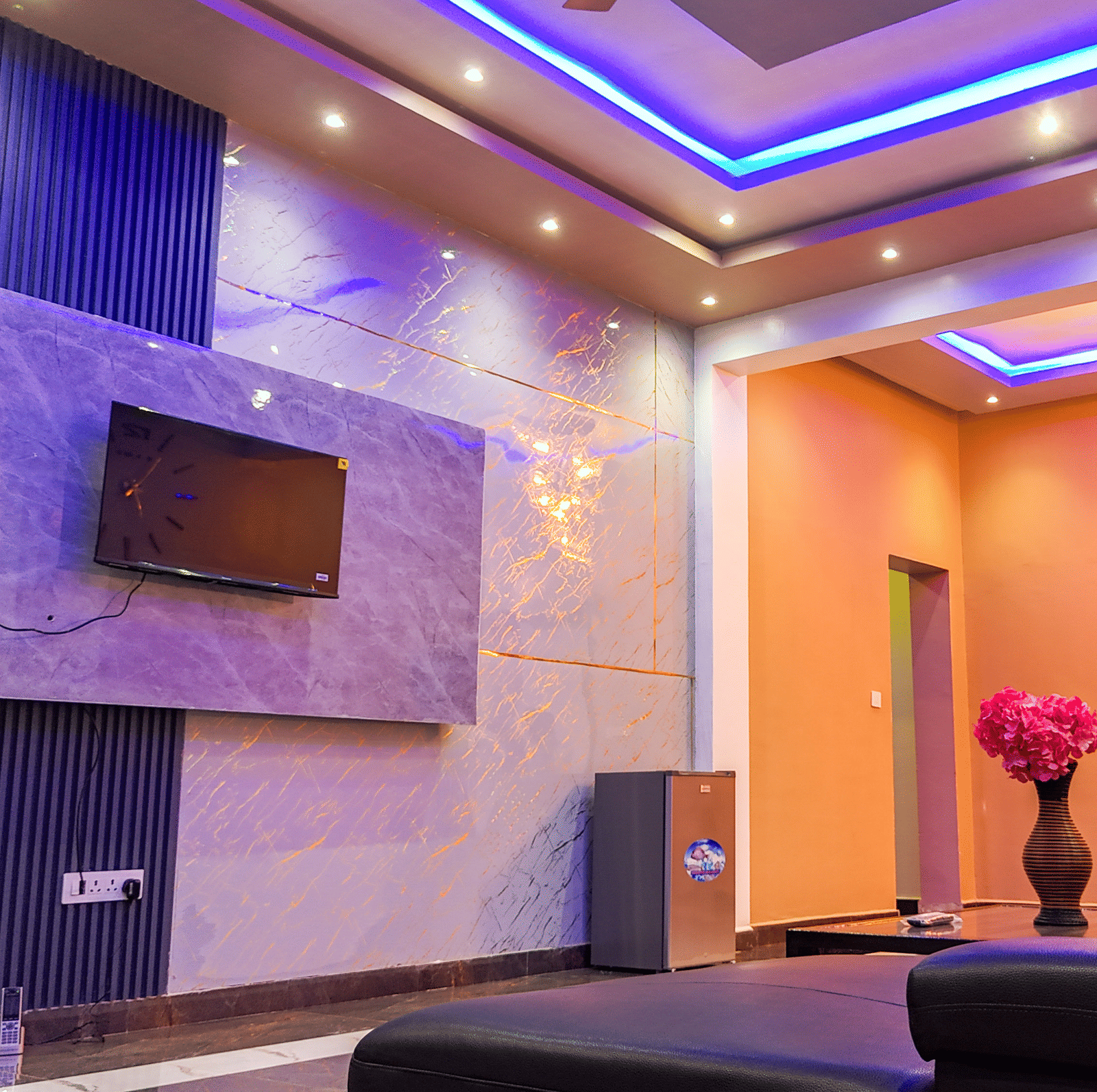 Living area with blue and purple accent lighting, a wall-mounted TV, and modern decor - Luffu Club
