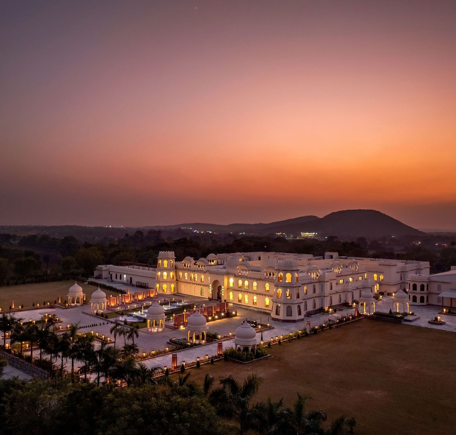 Aerial view of Kesar Bagh Palace illuminated with lights with mountains in the background.