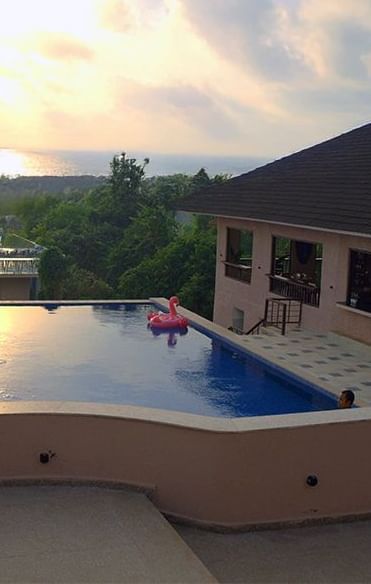nfinity pool at Crescent Resort, Goa with sunset sea view, a pink flamingo float, lush greenery, and poolside seating under soft evening sky.