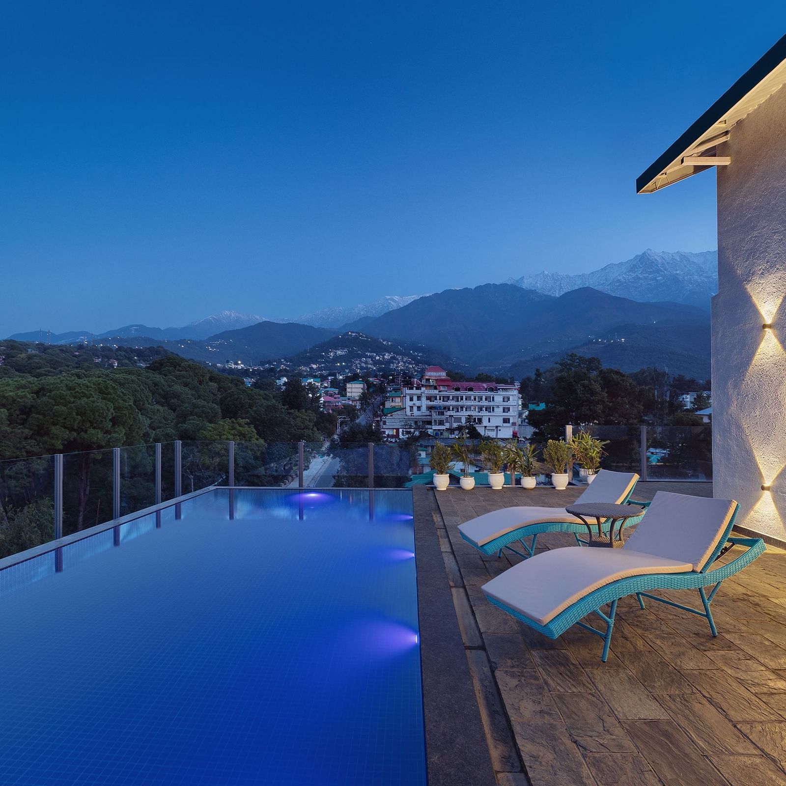 Rooftop pool lined with lounging chairs on a clear blue day with mountains in the backdrop