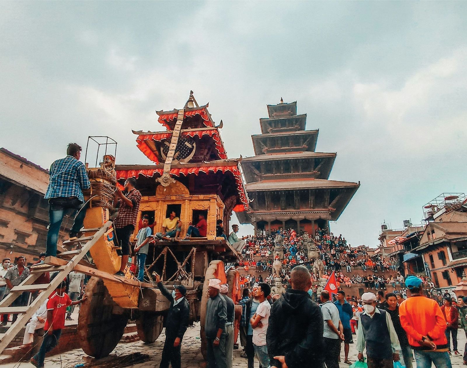 Traditional Nepali festival with a decorated chariot and a crowd gathered around a historical pagoda.