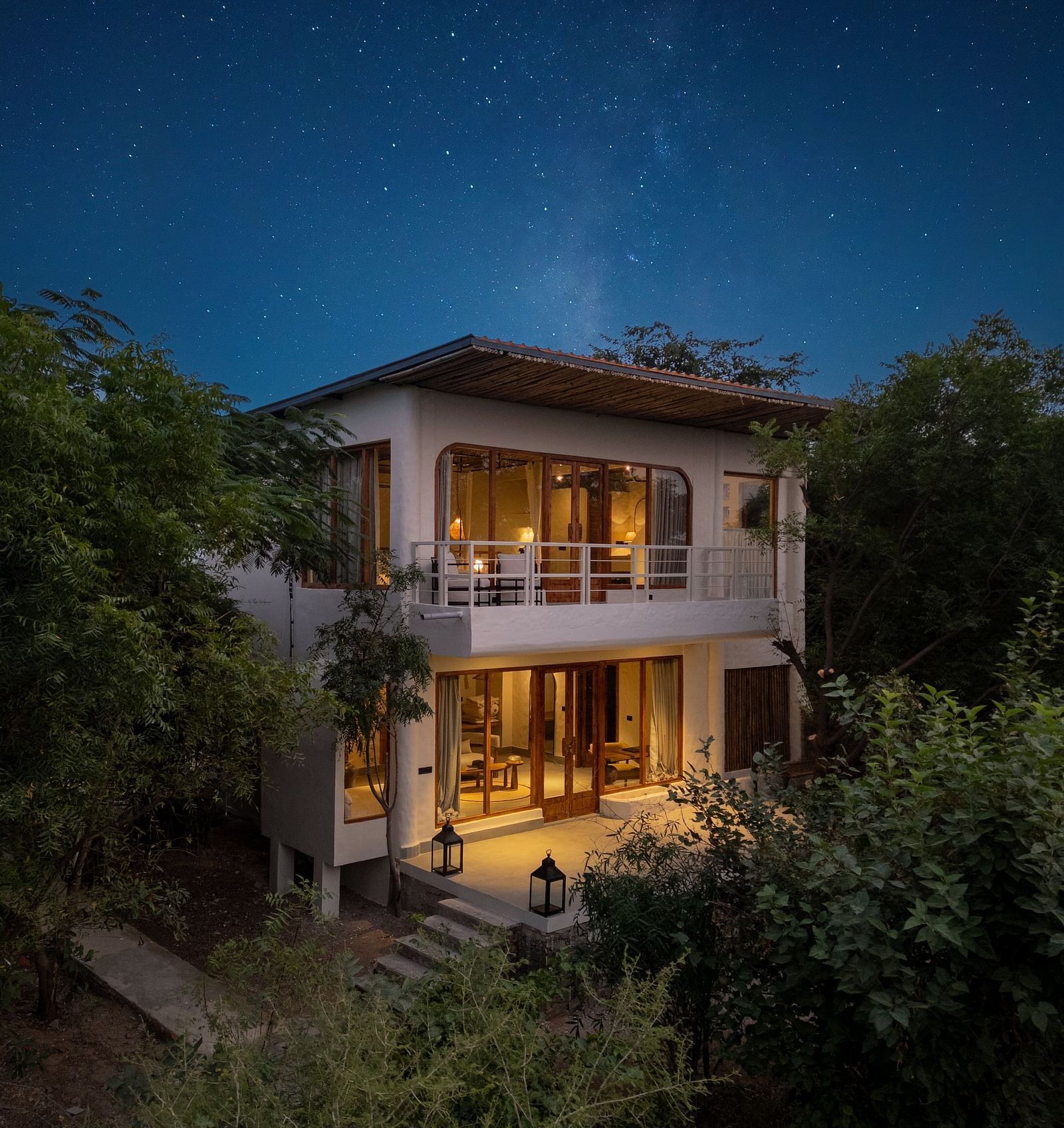 Exterior of a modern two-story villa surrounded by trees and plants.