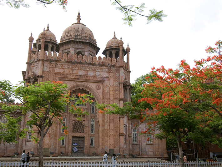 A large, ornate domed building surrounded by trees with red blossoms.
