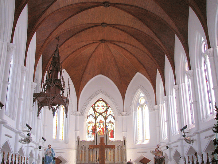 The vaulted interior of a large church with stained glass windows.