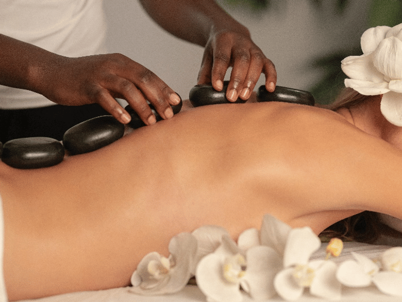 A therapist placing smooth black basalt stones along a woman's back, with white orchids beside her