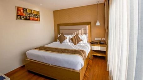 A bright and neatly arranged standard hotel room with a comfortable bed, a small desk, and an abstract painting above the bed at Yashshree The Imperial Inn, Siliguri.