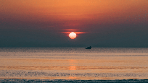 a beautiful view of the sun setting as seen from Radhangar beach with a boat also in view