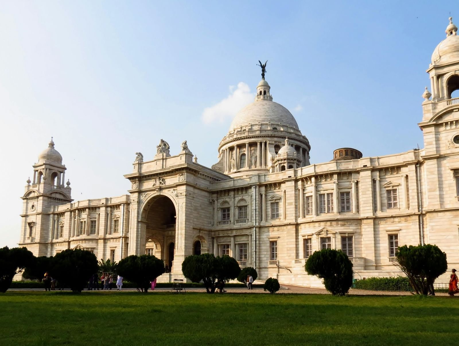 Facade of Victoria Memorial Hall in Kolkata with sprawling gardens and Renaissance-inspired architecture under a blue sky.
