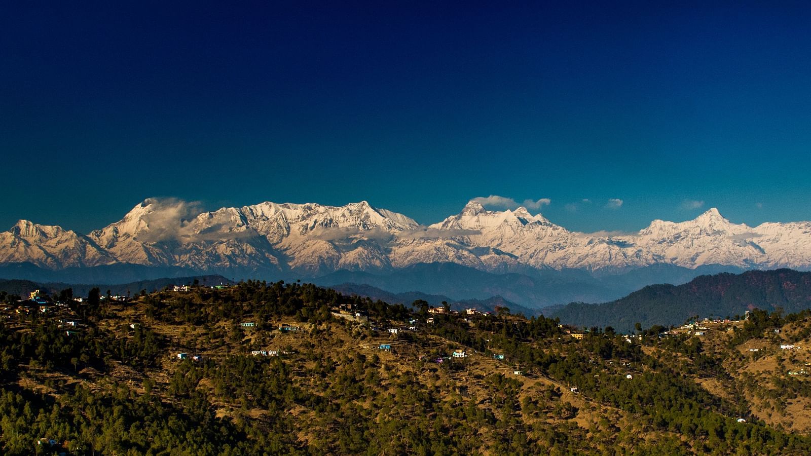 Scenic views of the Himalayas surrounded by lush greenery and set against the backdrop of rolling hills and blue skies.