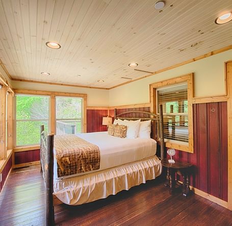 corner view image of a double bed overlooking amazing lush green views from the huge windows in front of it - Historic Tapoco Lodge