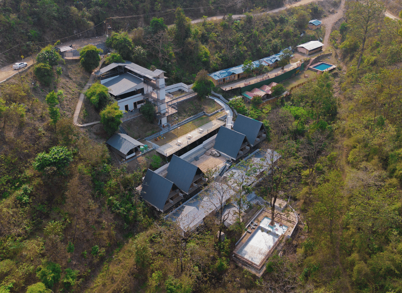 An aerial shot shows the buildings of Perfect Stayz The Jungle Resort surrounded by trees and hills.