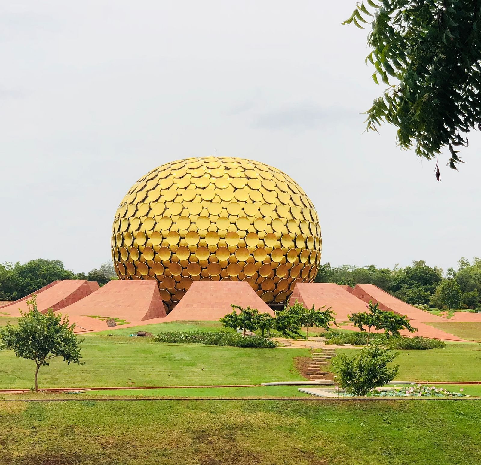 Wide view of Auroville golden building with a manicured garden in the foreground