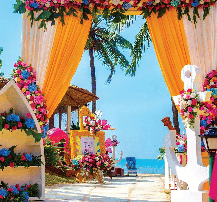 Vibrant Indian wedding mandap at Caravela Beach Resort Goa with colorful floral decorations, orange drapes, and ocean backdrop