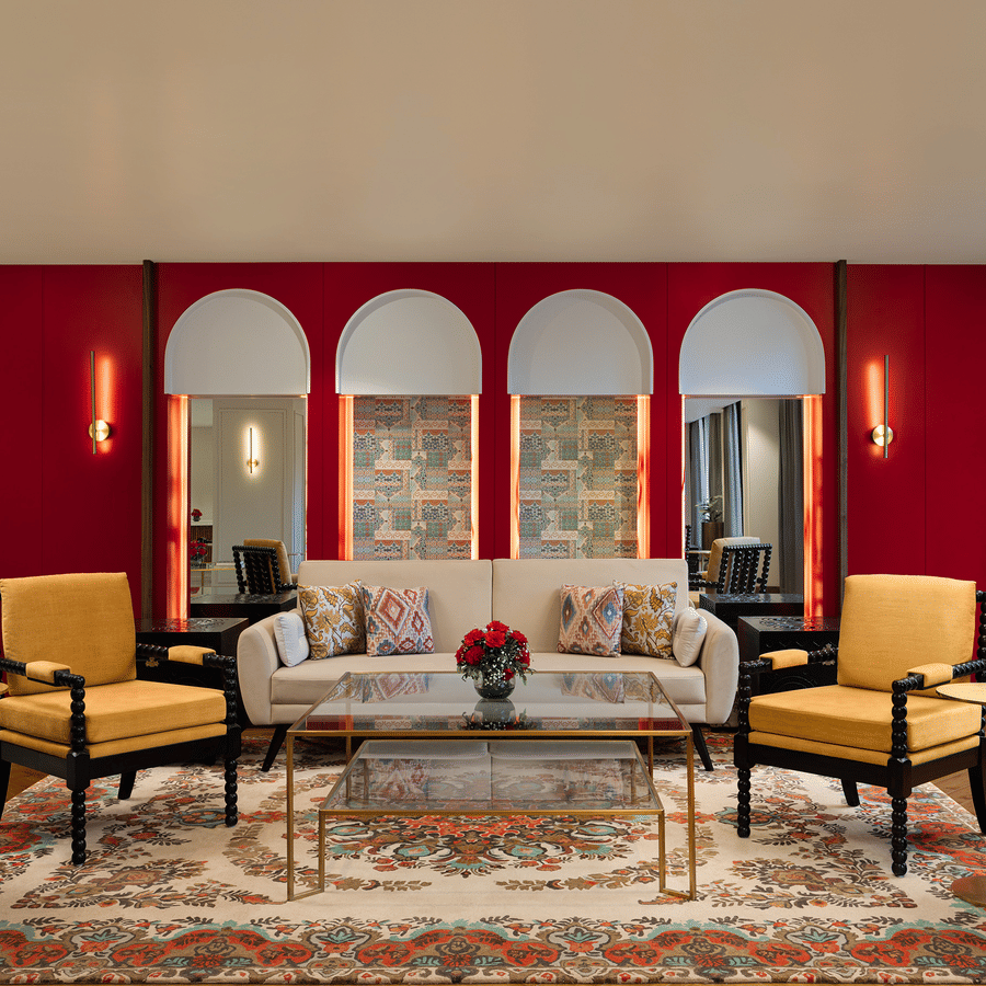 Elegant lounge area with a red feature wall, four arched mirrors, yellow armchairs, and a traditional patterned rug.