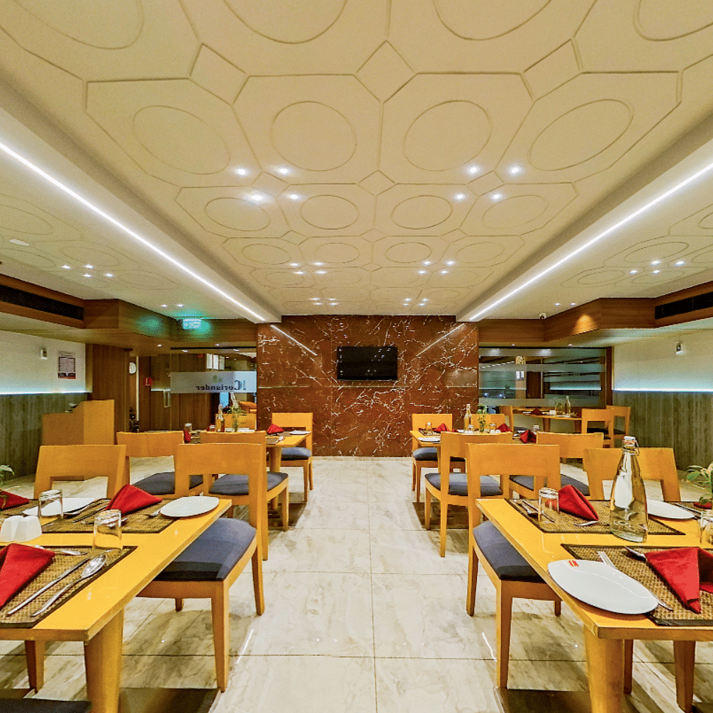 Contemporary restaurant with wooden dining tables, black chairs and red napkins at Lords Eco Inn Dahej, set for guest dining service