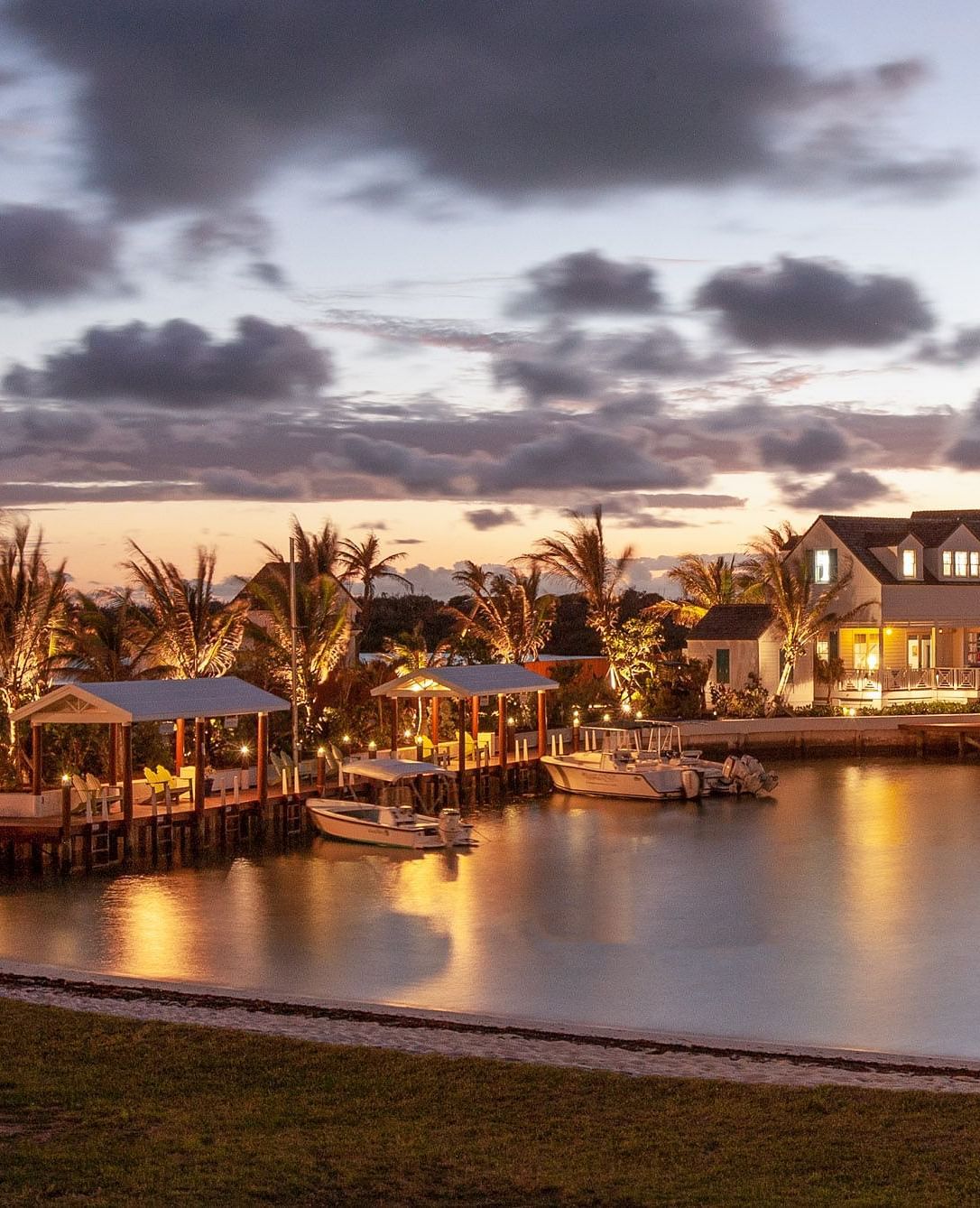 Waterfront buildings glow under dramatic evening skies, with lights reflecting off the calm water in a twilight setting | Abaco Inn