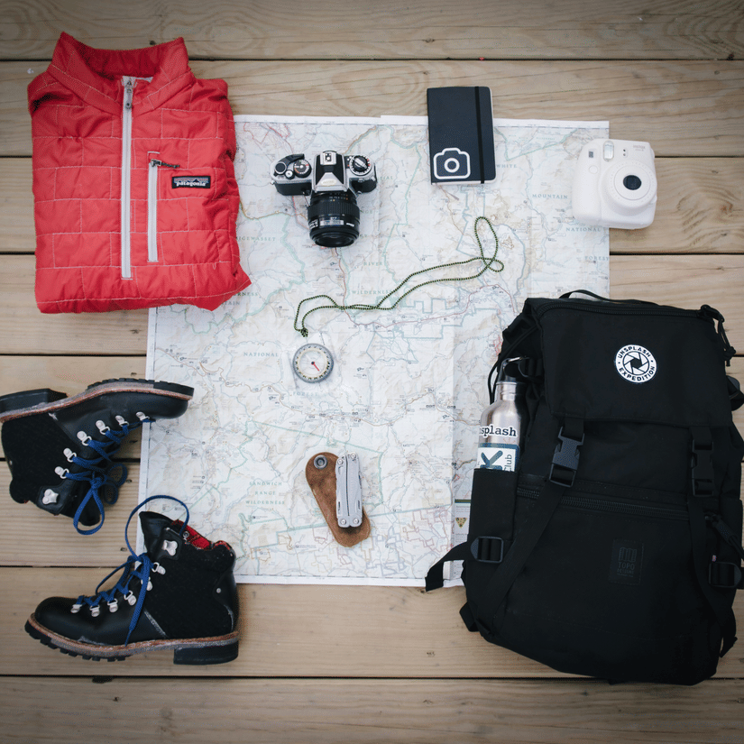 Trekking gear kept neatly next to each other, including a map, boots, a jumper, camera, and abag