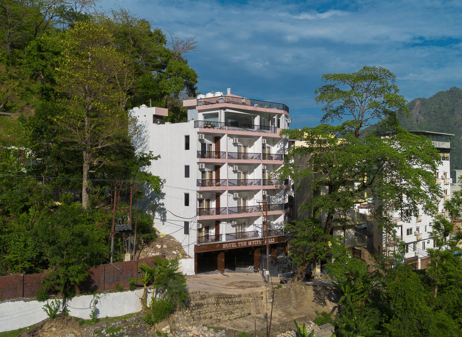 An exterior of a building with multiple storeys, balconies, and windows, surrounded by trees on a hillside in Perfectstayz Premium Mystic Falls, Rishikesh.