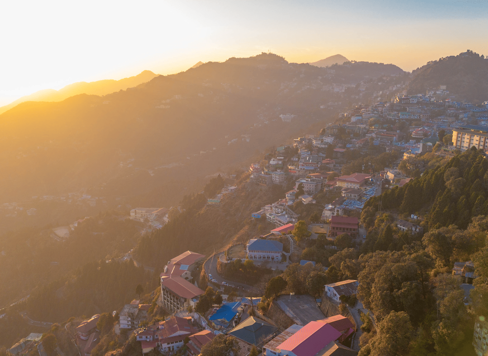 A panoramic view of a mountain town built on rolling hills, bathed in the golden light of sunrise or sunset | Perfectstayz Value Valley Vista