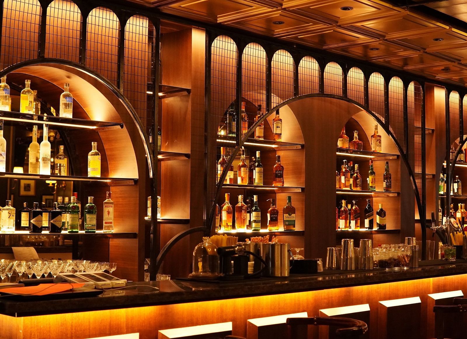 A dimly lit bar with a wooden counter, shelves filled with bottles of liquor, and warm lighting.