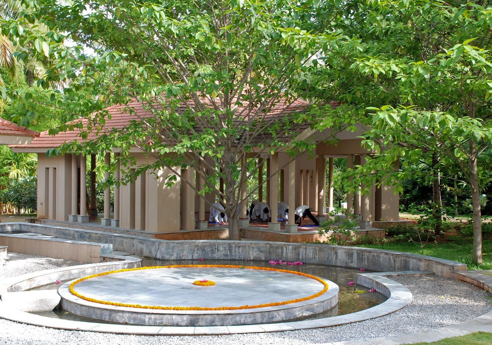 A circular feature surrounded by trees and a building with a thatched roof, outdoor setting - Shreyas Retreat