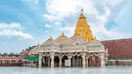 A large, intricate temple with a gold and white exterior, with a cloudy sky.