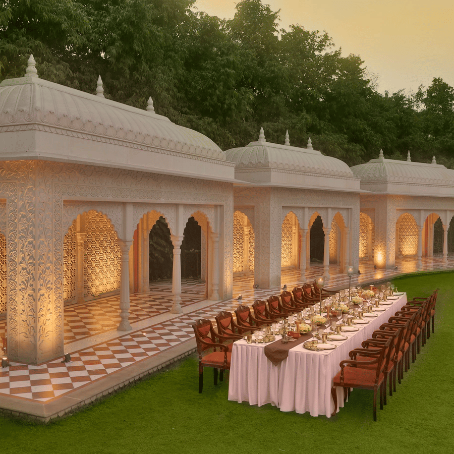 Elegantly set long dining table under ornate, domed structures on a green lawn at dusk at Heritage Village Resorts & Spa.