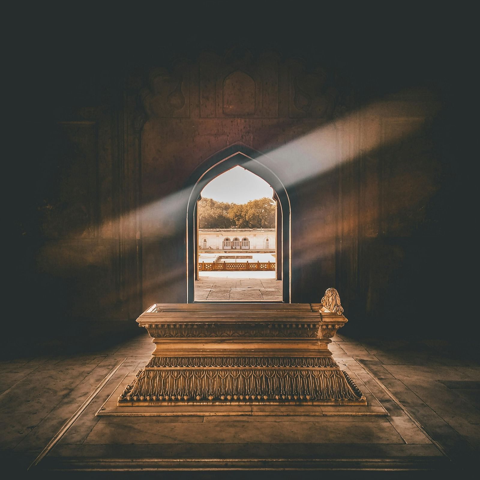 A dramatic view inside a historical building with a sunbeam streaming through an arched doorway, illuminating an ornate golden tomb.