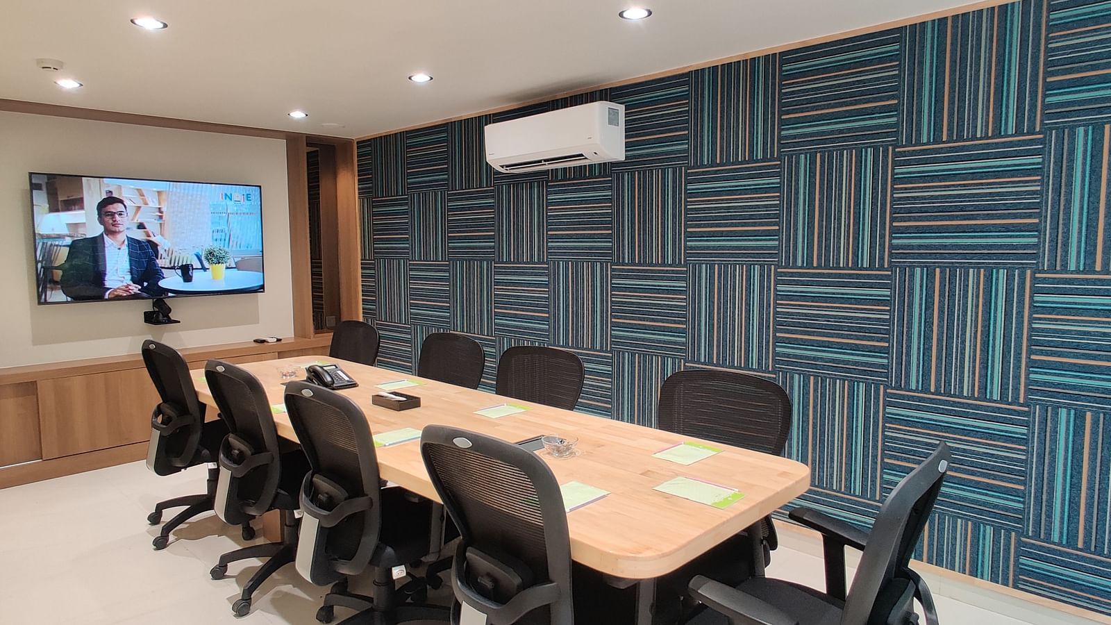 A boardroom with a large rectangular table surrounded by chairs, and a large wall-mounted TV at Indie Stays
