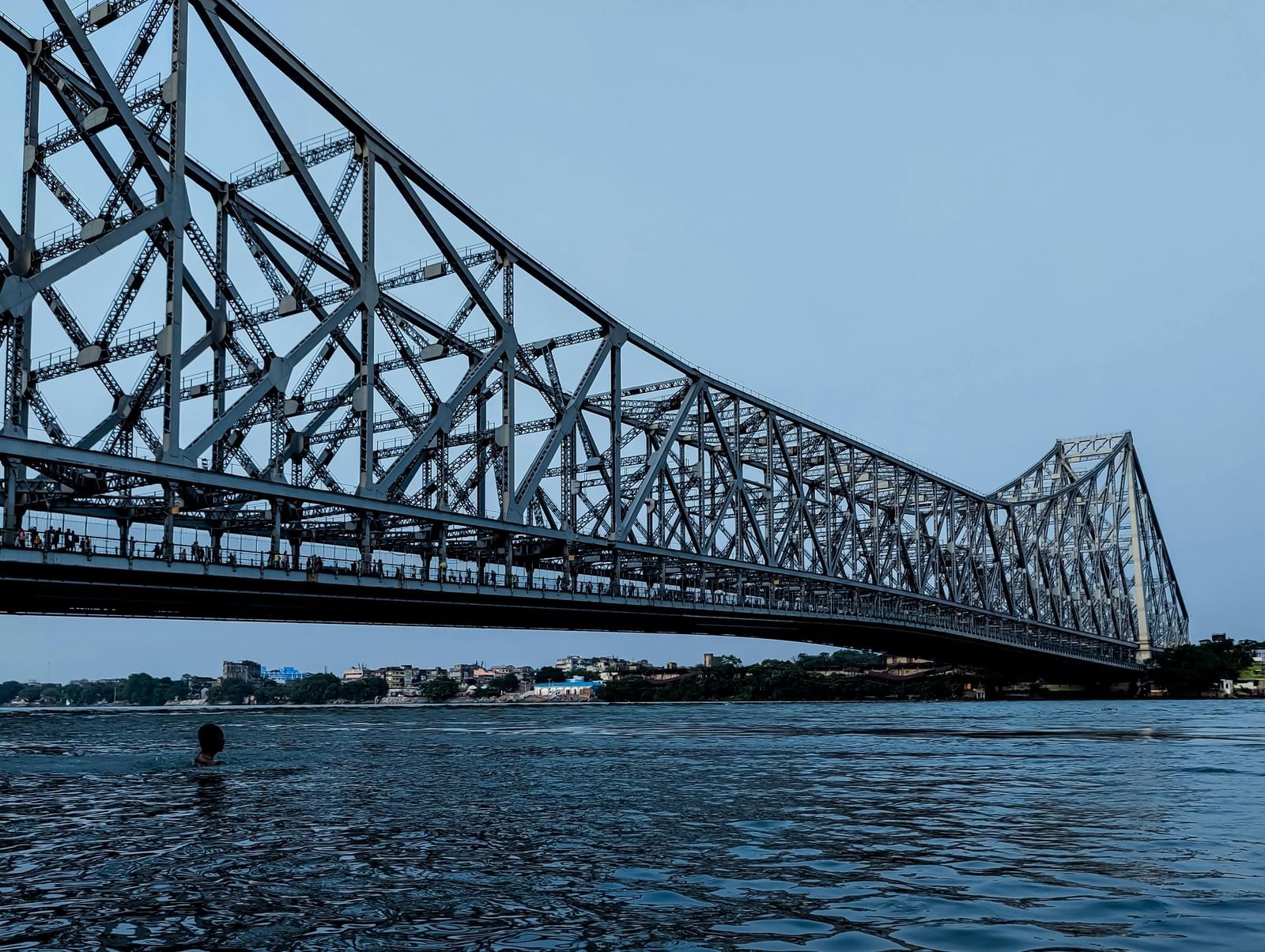 Distant view of Howrah Bridge spanning over the Hooghly River with water flowing beneath.
