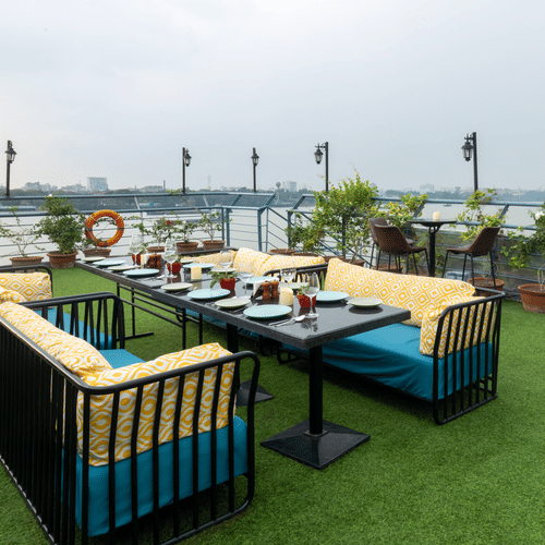  An outdoor dining setup on a rooftop garden overlooking a bridge and river during daylight - Polo Floatel