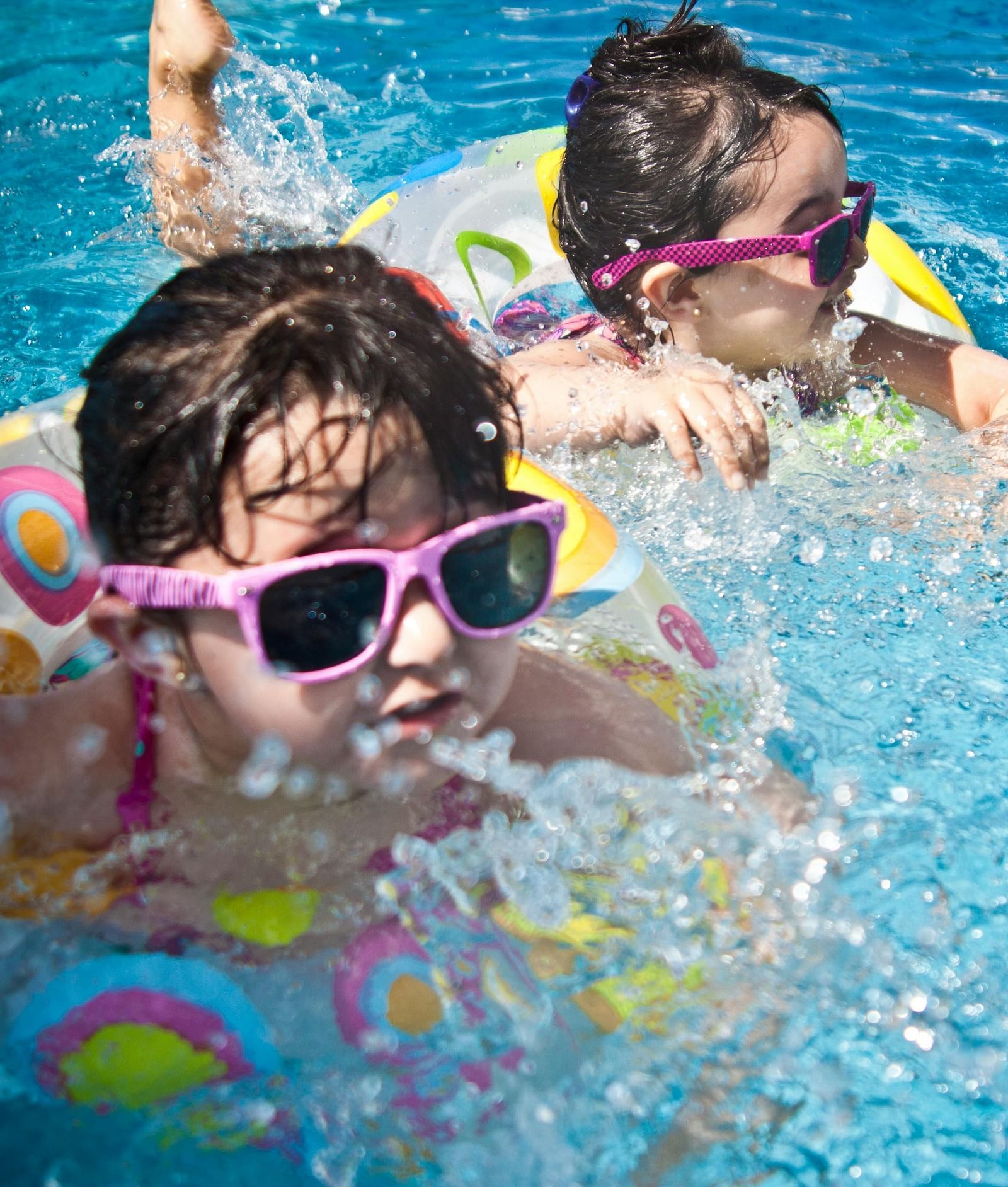 Two kids playing in the swimming pool, both wearing floaties