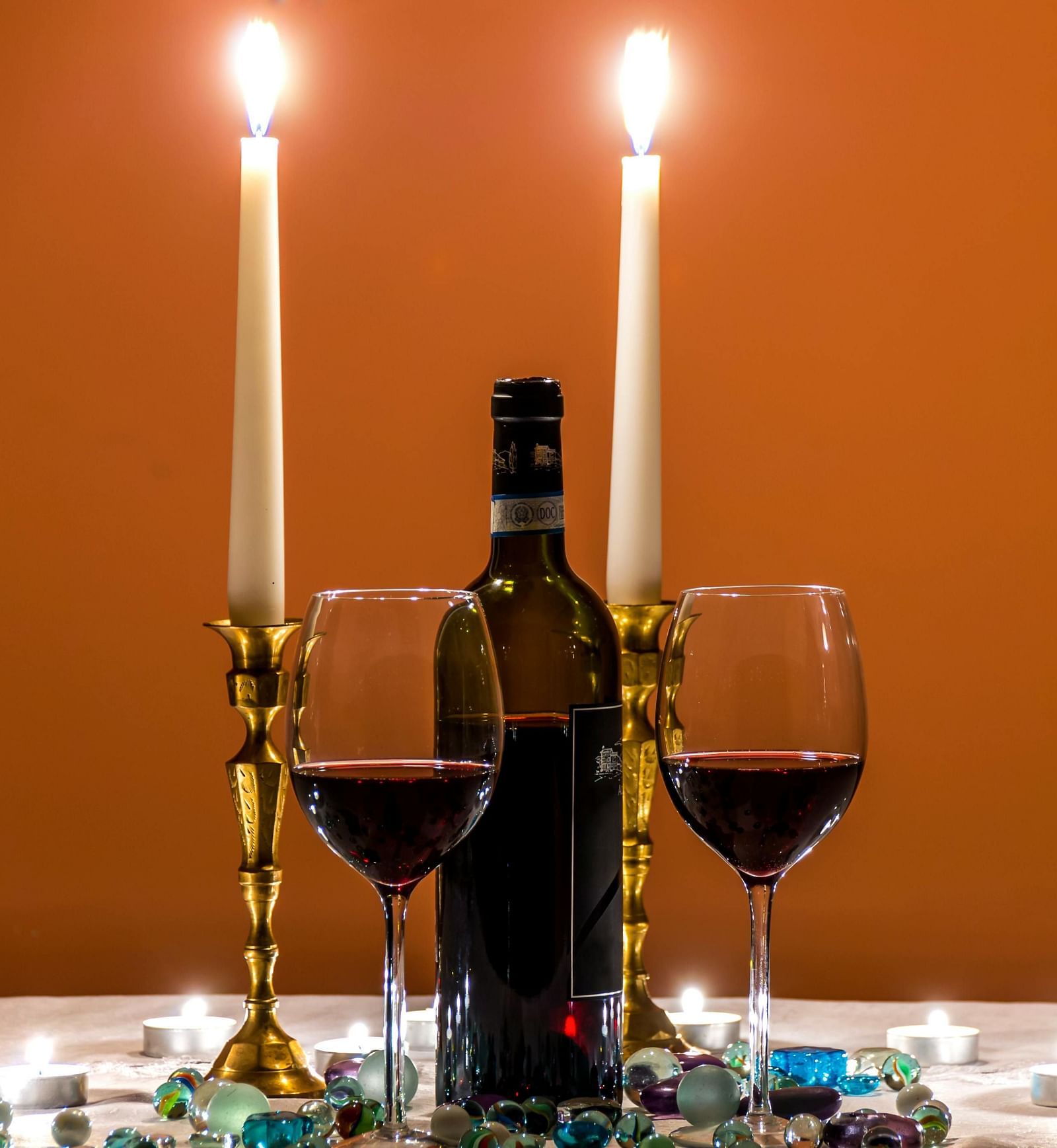Romantic ambience created by candlelight, two glasses of red wine, and a wine bottle against a warm orange backdrop
