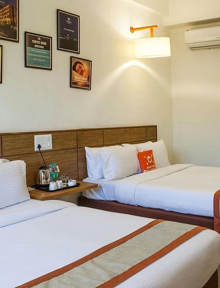 full view image of the max family room featuring two plush double beds along with a split air-conditioner and a bedside table between the two beds - Max Hotel Jabalpur