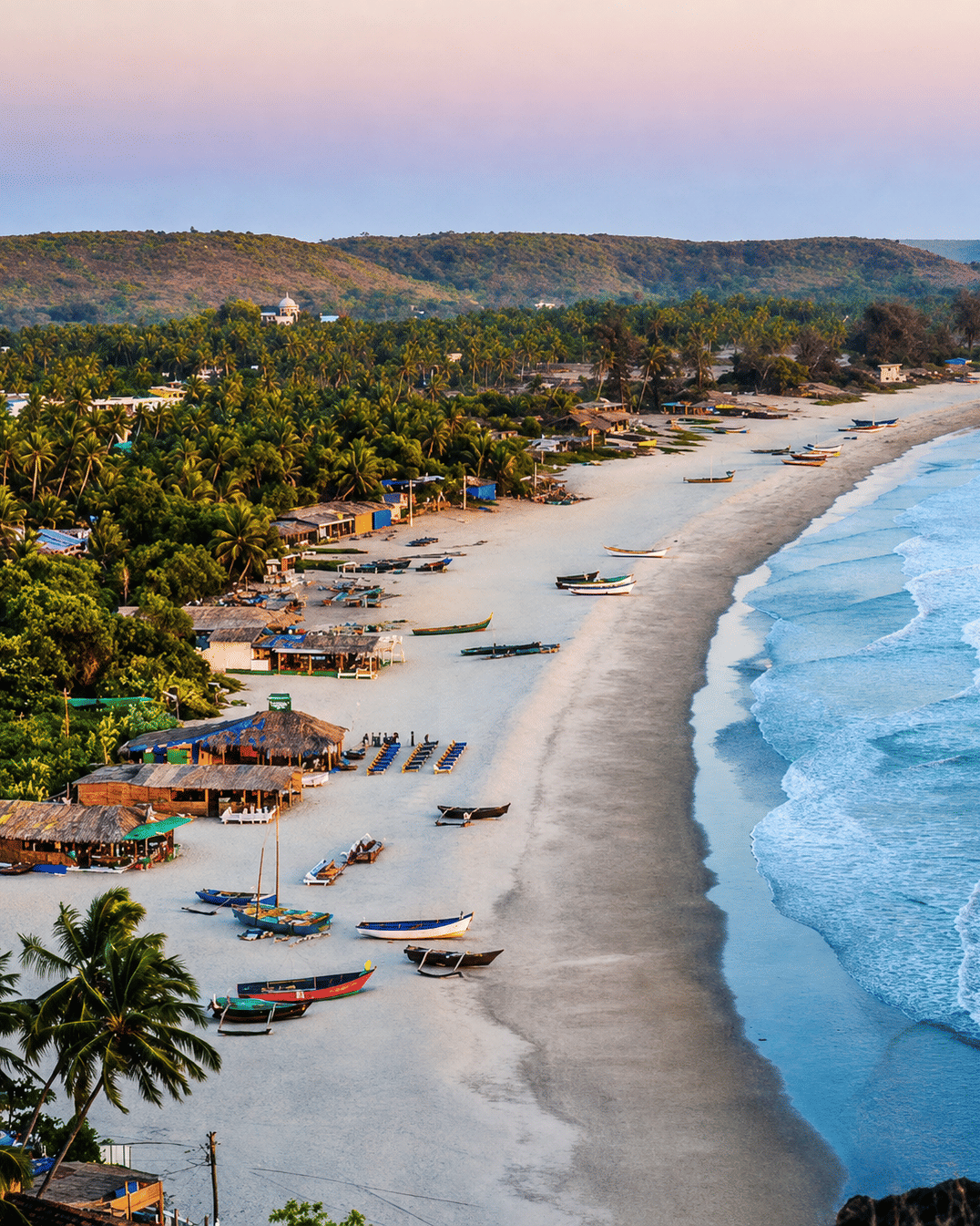 Aerial view of North Goa coastline with a sandy beach, blue Arabian Sea, palm trees and lush greenery along the shore.