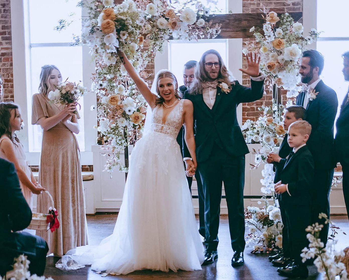  A joyful wedding ceremony with the bride and groom standing in front of their guests, exchanging vows amidst beautiful floral arrangements.
