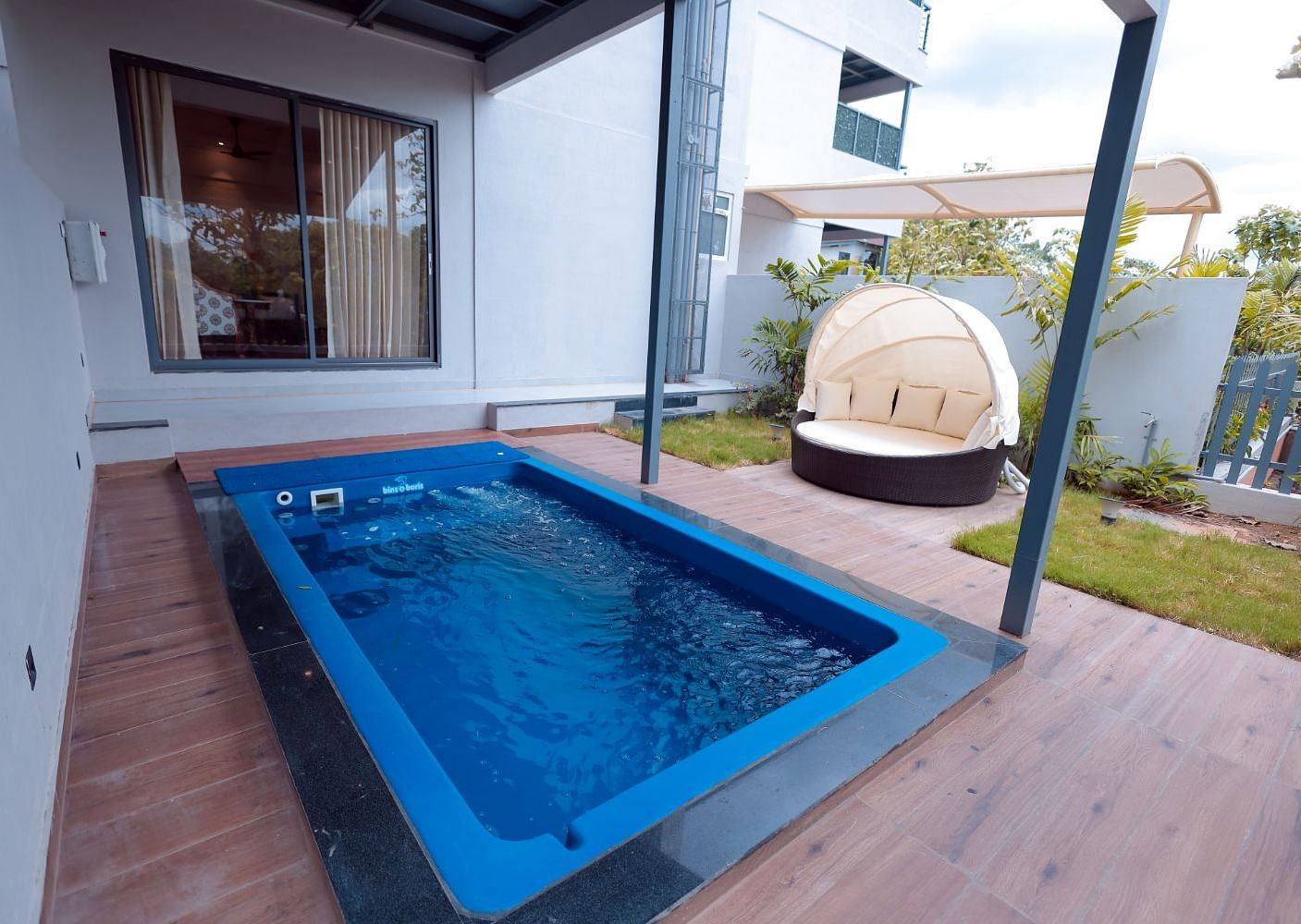 A Swimming pool beside the room surrounded by trees at A bedroom with two single cot, fan and warm lights at Trishvam Symphony, Krishnagiri.
