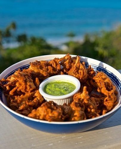 Bowl of fried snacks with green dipping sauce, placed outdoors with a blurred ocean view | A Stone's Throw Away