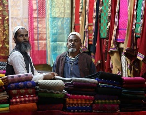 An image of two men with clothes hanging behind them and folded garments arranged in front.