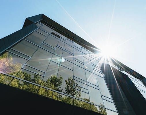 Modern building with reflective facade under a bright sky with trees being visible in the reflections.
