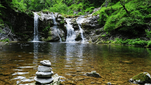A shot at the Jalagamparai Waterfalls with stone cairn on the water body, and  the waterfall amidst the canopy.